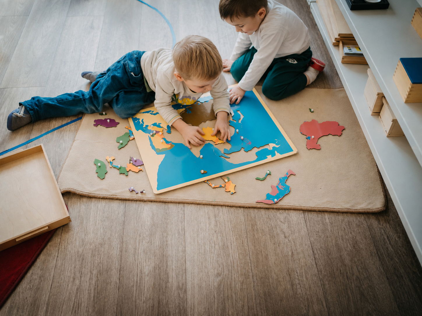 Deux enfants assemblent ensemble le puzzle de la carte du monde, allongés sur un tapis