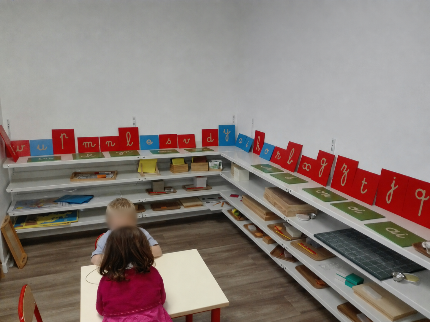 Photo d'archives : deux enfants travaillent à une table devant les étagères garnies de lettres rugueuses rouges et bleues