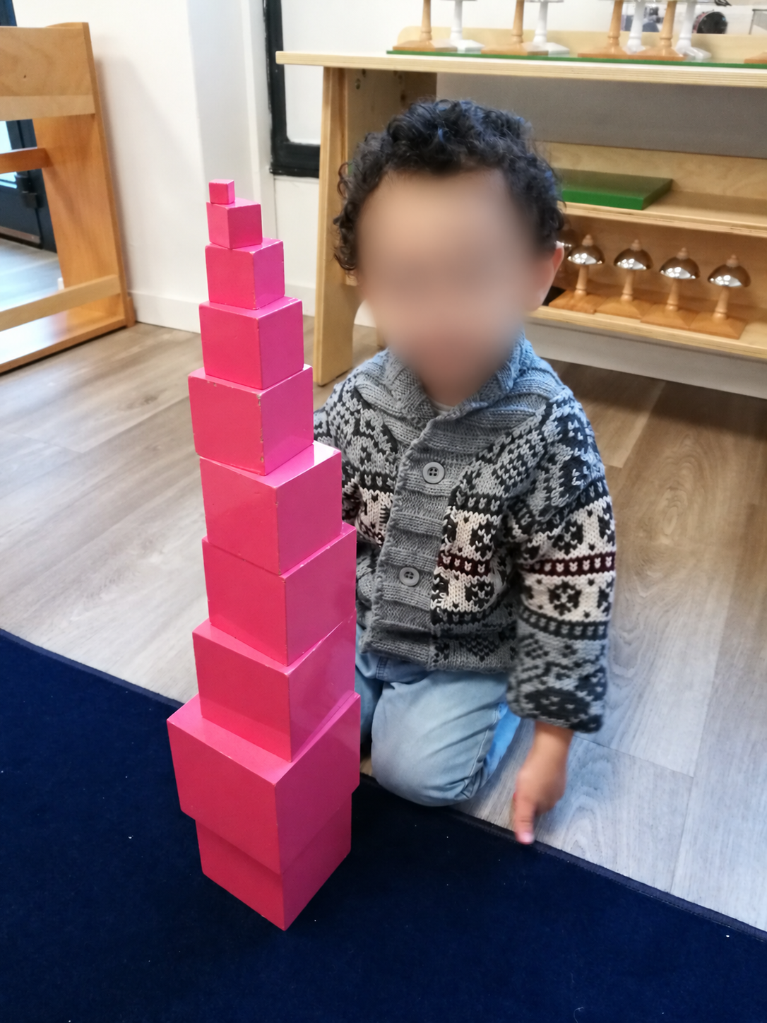 Photo d'archives : un enfant agenouillé sur un tapis à côté de la tour rose qu'il vient de construire
