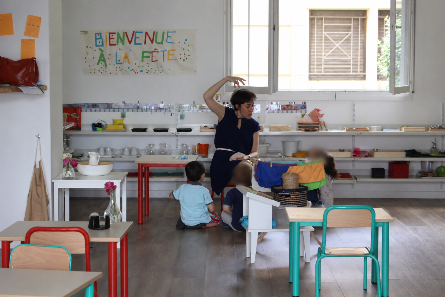 Photo d'archives : une éducatrice étend du linge avec trois enfants dans la classe, sous une banderole « Bienvenue à la fête »