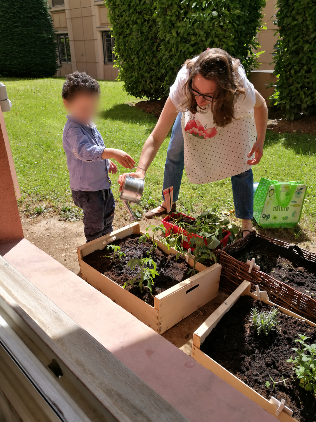 Photo d'archives : un enfant arrose les plants d'un carré potager avec l'aide d'une éducatrice, dans le jardin