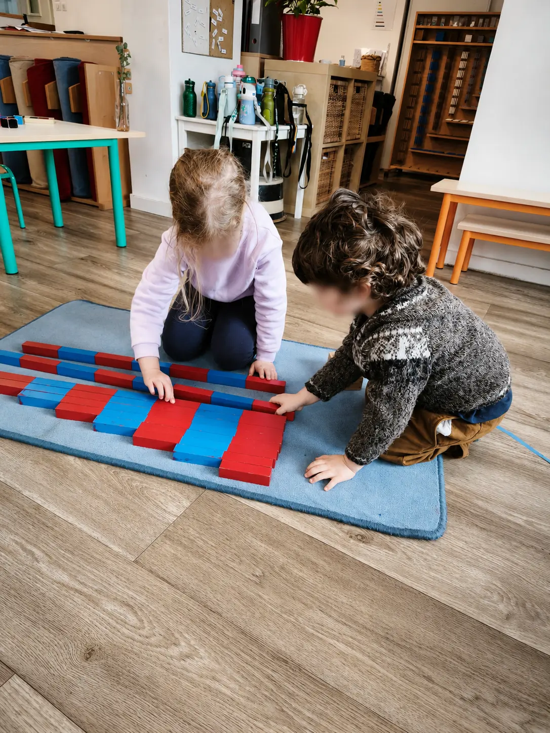 Deux enfants agenouillés sur un tapis alignent ensemble les barres rouges et bleues de numération