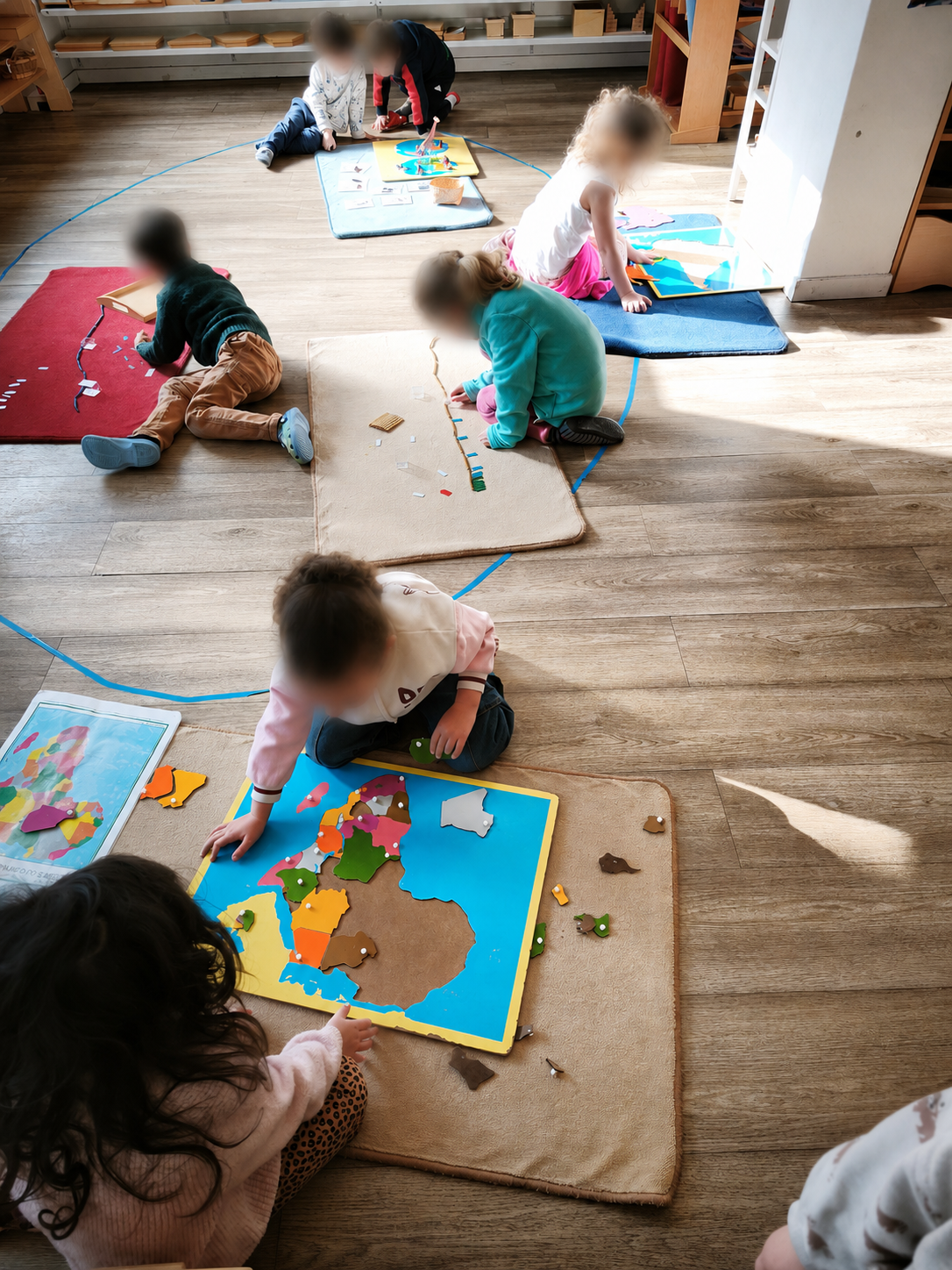 Plusieurs enfants travaillent au sol sur leurs tapis, dont l'un assemble le puzzle de la carte d'Afrique