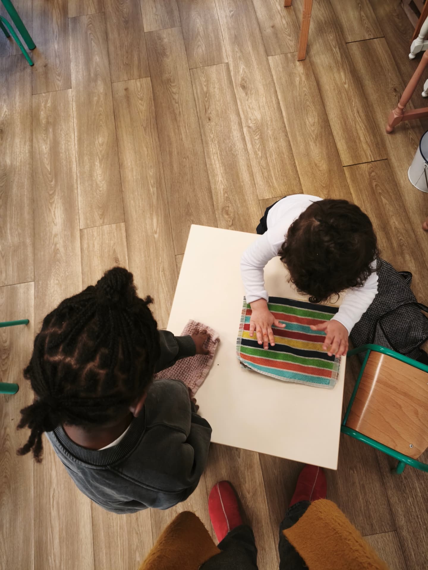 Deux enfants essuient ensemble une petite table avec des serviettes en tissu
