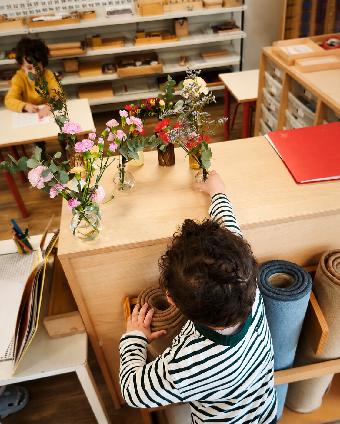 Une main d'enfant arrange le bouquet de fleurs préparé sur une petite table de la classe