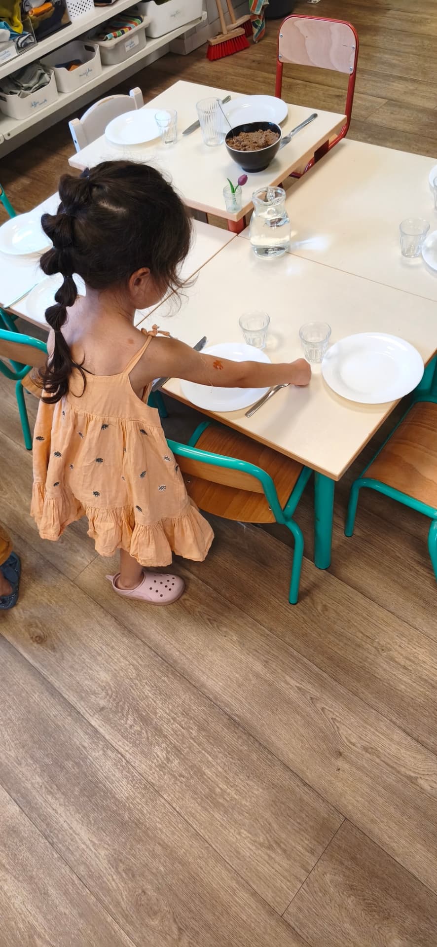 Une enfant en robe pêche dispose les assiettes et les verres sur les tables avant le déjeuner
