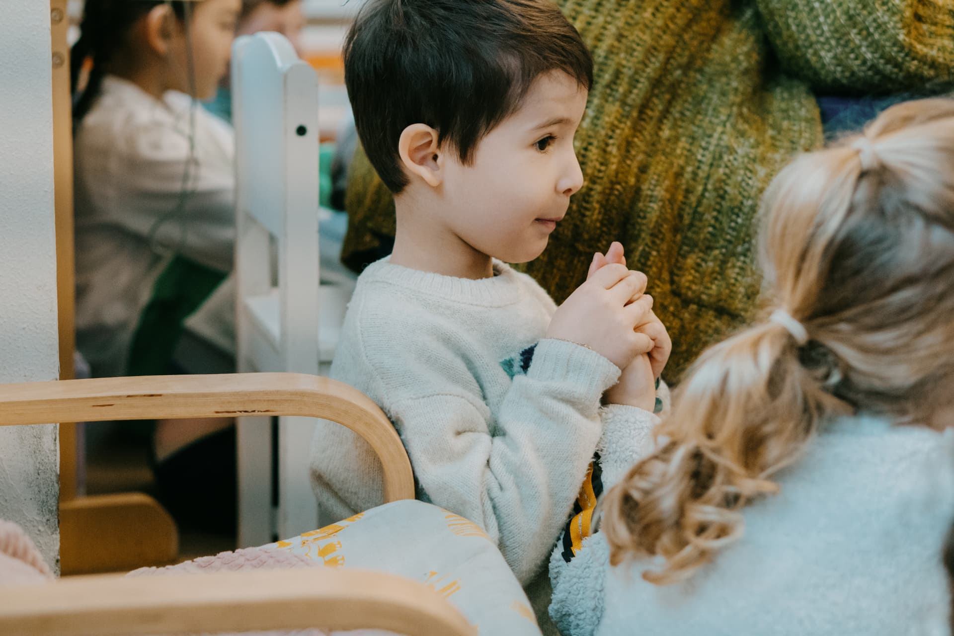 Un enfant attentif, les mains jointes, pendant un temps d'échange dans la classe