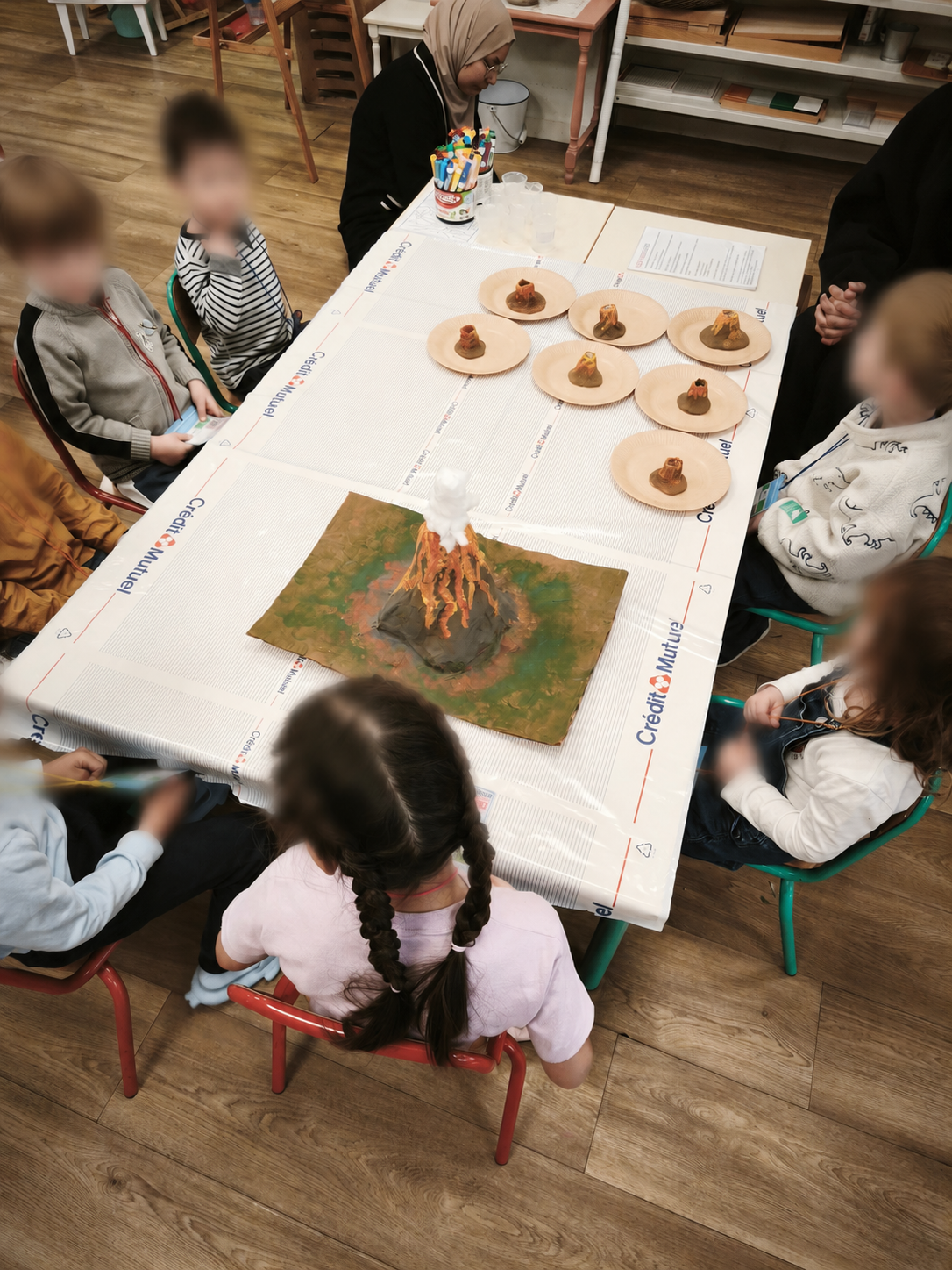 Des enfants réunis autour d'une grande table observent une maquette de volcan en éruption