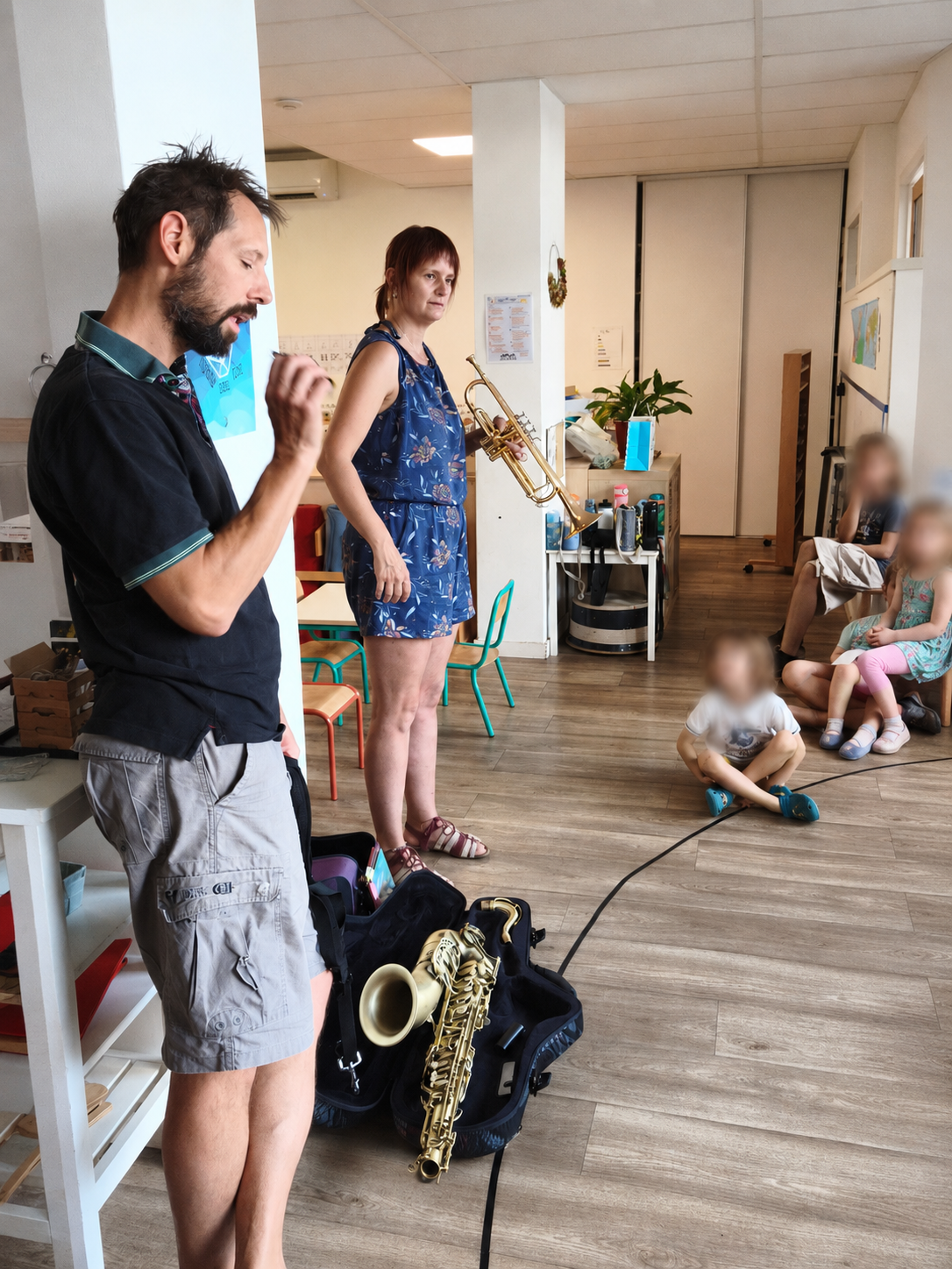 Deux musiciens présentent une trompette et un saxophone aux enfants assis dans la classe