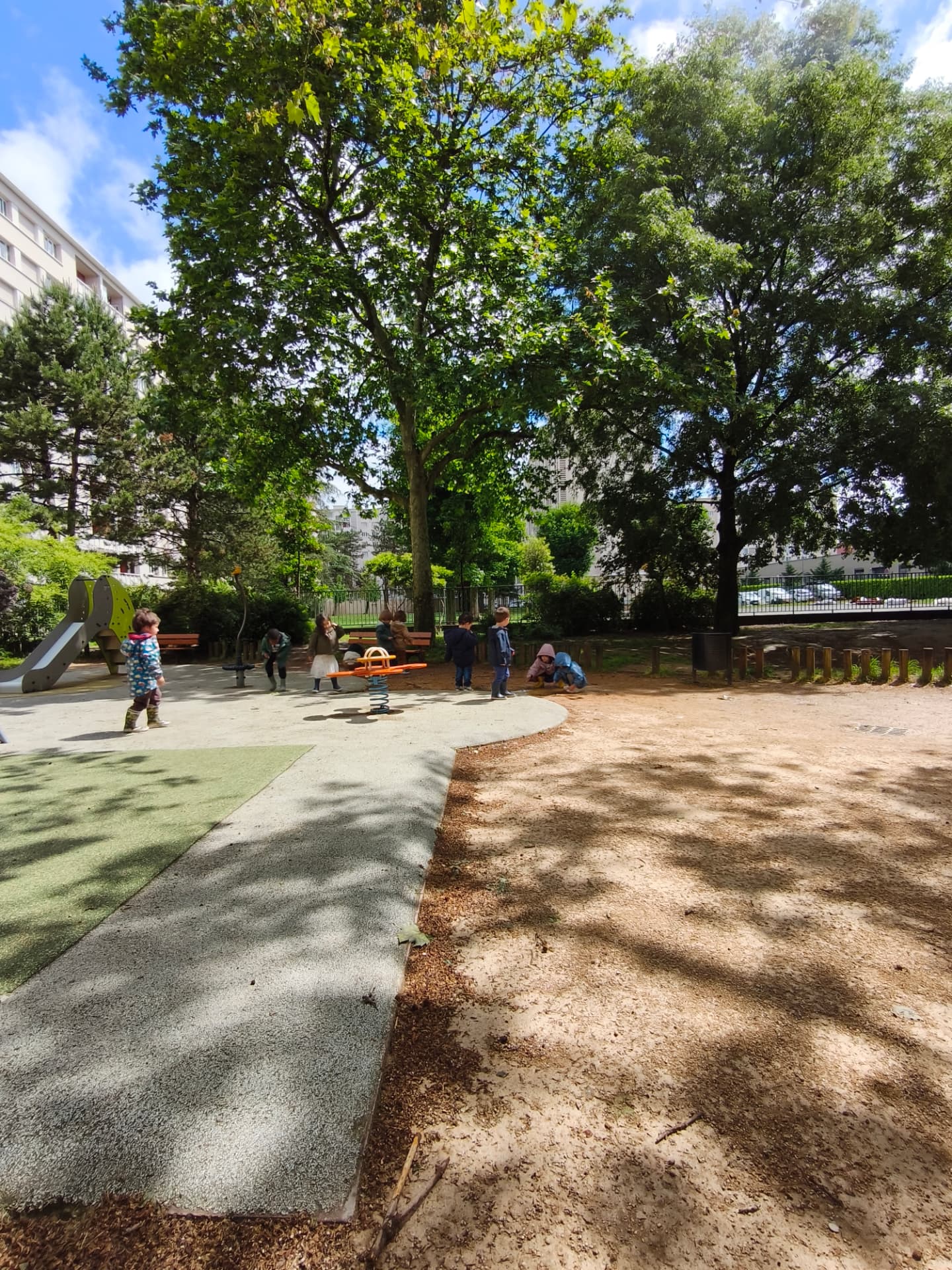 Des enfants jouent dans le square ombragé, sous les grands arbres, un matin de printemps